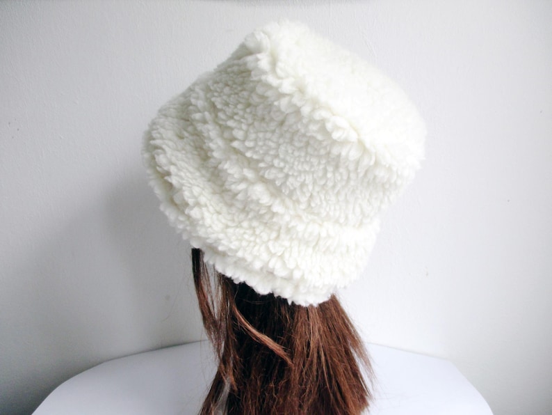 Puede incluir: Un gorro de cubo blanco y esponjoso hecho de tela suave y texturizada.