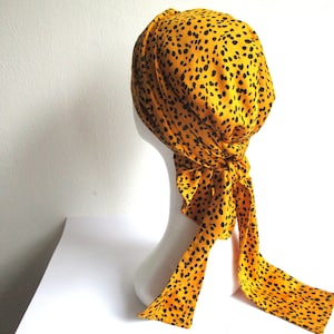 Pode incluir: Um turbante amarelo e preto estampado com uma cauda longa. O turbante &eacute; feito de um tecido macio e tem um ajuste confort&aacute;vel.