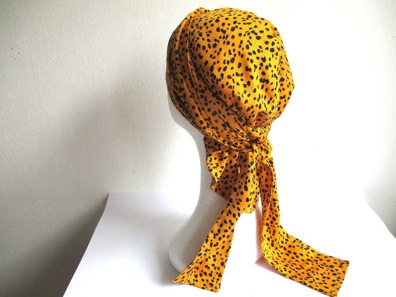 Pode incluir: Um turbante amarelo e preto estampado com uma cauda longa. O turbante &eacute; feito de um tecido macio e tem um ajuste confort&aacute;vel.
