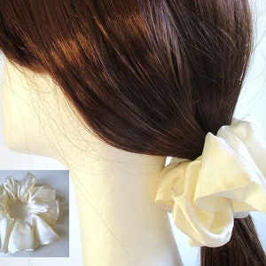 May include: A white satin scrunchie for hair. The scrunchie is made of soft, gathered fabric and is tied in a knot.