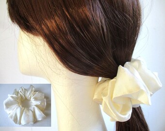 May include: A white satin scrunchie for hair. The scrunchie is made of soft, gathered fabric and is tied in a knot.