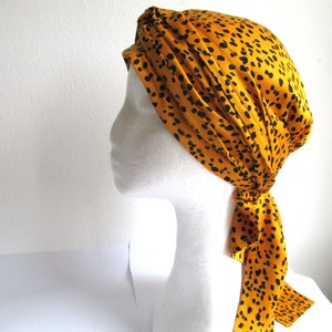 Pode incluir: Um turbante de cetim amarelo e preto com padr&atilde;o e uma longa gravata. O turbante est&aacute; amarrado em uma cabe&ccedil;a de manequim branca.