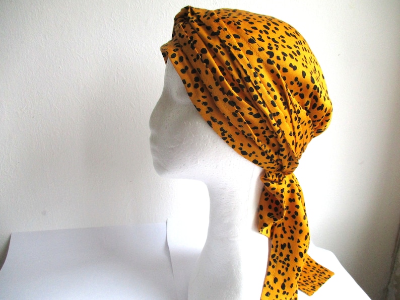 Pode incluir: Um turbante de cetim amarelo e preto com padr&atilde;o e uma longa gravata. O turbante est&aacute; amarrado em uma cabe&ccedil;a de manequim branca.
