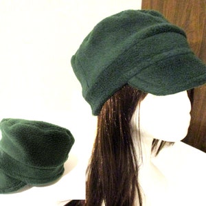 Peut inclure: Une casquette de newsboy en polaire vert foncé avec une visière. La casquette est pliée vers le bas à l'avant et a une coupe légèrement ample.