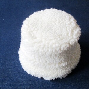 Puede incluir: Un gorro de cubo blanco y peludo. El gorro est&aacute; hecho de un material suave y afelpado.