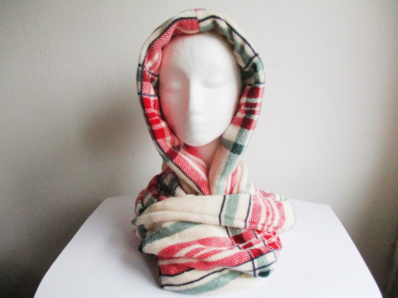 May include: A red, white and green plaid scarf with a white fleece lining. The scarf is folded and tied around a mannequin's neck.