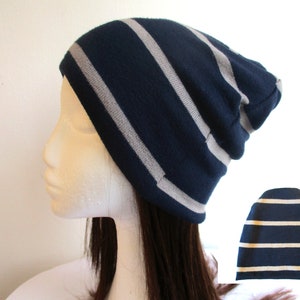May include: A navy blue and gray striped beanie hat. The hat is folded down and has a slouchy fit.