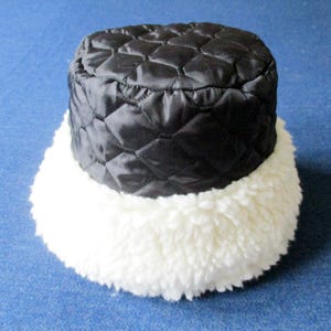 Puede incluir: Un gorro de cubo acolchado negro con un borde de piel sint&eacute;tica blanca.