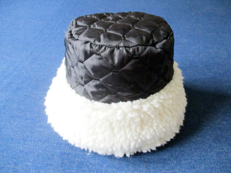 Puede incluir: Un gorro de cubo acolchado negro con un borde de piel sint&eacute;tica blanca.