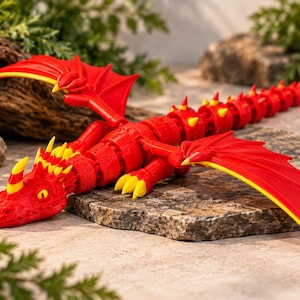 May include: A red articulated dragon figurine featuring bright yellow accents on its horns, claws, and wing tips. The creature has a textured, segmented body with a long tail and outstretched wings, designed with a flexible structure.