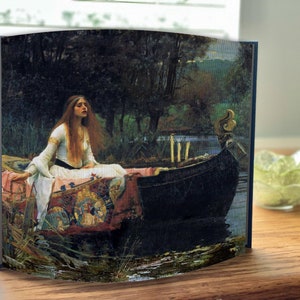 Puede incluir: Una pintura de una mujer con un vestido blanco sentada en un bote en un lago. La mujer tiene el pelo largo y castaño y mira hacia abajo. El bote es azul oscuro y tiene ribetes dorados. El lago está rodeado de árboles y hay una puesta de sol en el fondo.