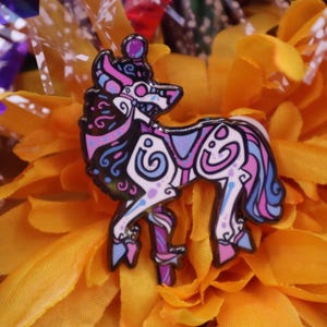 May include: A decorative pin featuring a stylized horse design with black, white, blue, and pink accents. The pin is set against a backdrop of bright yellow flowers, creating a vibrant contrast. The horse design has intricate patterns and a glossy finish.