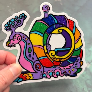 May include: A die-cut sticker featuring a stylized snail with a glittery, rainbow-colored shell and a purple body. The snail has intricate black outlines, a swirling antenna structure, and vibrant segments of red, orange, yellow, green, and blue.
