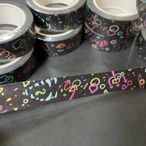 May include: A roll of black washi tape with a colorful geometric pattern. The tape features neon pink, green, blue, and yellow shapes and lines.