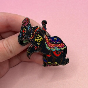 May include: A black enamel pin shaped like a carousel horse with intricate colorful patterns in red, blue, yellow, and teal. The design features a yellow infinity heart symbol on the flank, a saddle with a pi symbol, and decorative swirls.
