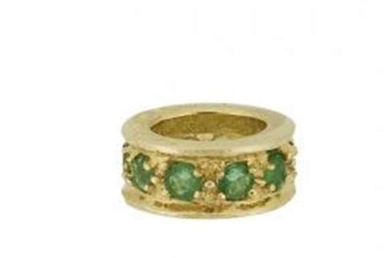 May include: A gold ring with a band of emerald green gemstones.