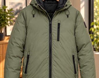 May include: A sage green hooded jacket featuring a black interior lining, a full-length black front zip, two lower zipped pockets, and one vertical zipped chest pocket. The jacket includes black ribbed cuffs and a drawstring hood.