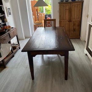 May include: A rectangular dark brown wooden dining table with a smooth, polished surface and four straight, tapered legs. The table features a solid wood construction with visible grain patterns and a simple, functional design for seating.