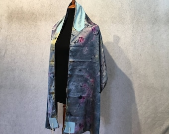 May include: A gray and blue prayer shawl with a light blue trim and white tassels. The shawl is displayed on a wooden mannequin.