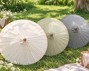 May include: Three circular paper parasols with wooden handles, arranged in a row. The parasols are colored in off-white, light sage green, and slate gray, each featuring a pleated center hub and a delicate, textured paper canopy surface.