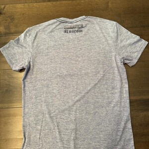 May include: A grey marl t-shirt with short sleeves and a dark blue trim around the crew neck. The text "Von Dutch Kustom" is printed across the upper back of the shirt in dark blue.