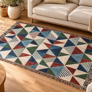 May include: A rectangular woven throw blanket featuring a geometric pattern of triangles in shades of dark blue, light blue, forest green, and deep red on a cream background, finished with a fringed edge on all four sides.