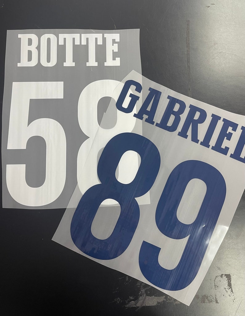 Puede incluir: Dos transferencias de planchado blancas con el texto "BOTTE" y los n&uacute;meros "58" en una transferencia y el texto "GABRIEL" y los n&uacute;meros "89" en la otra transferencia.