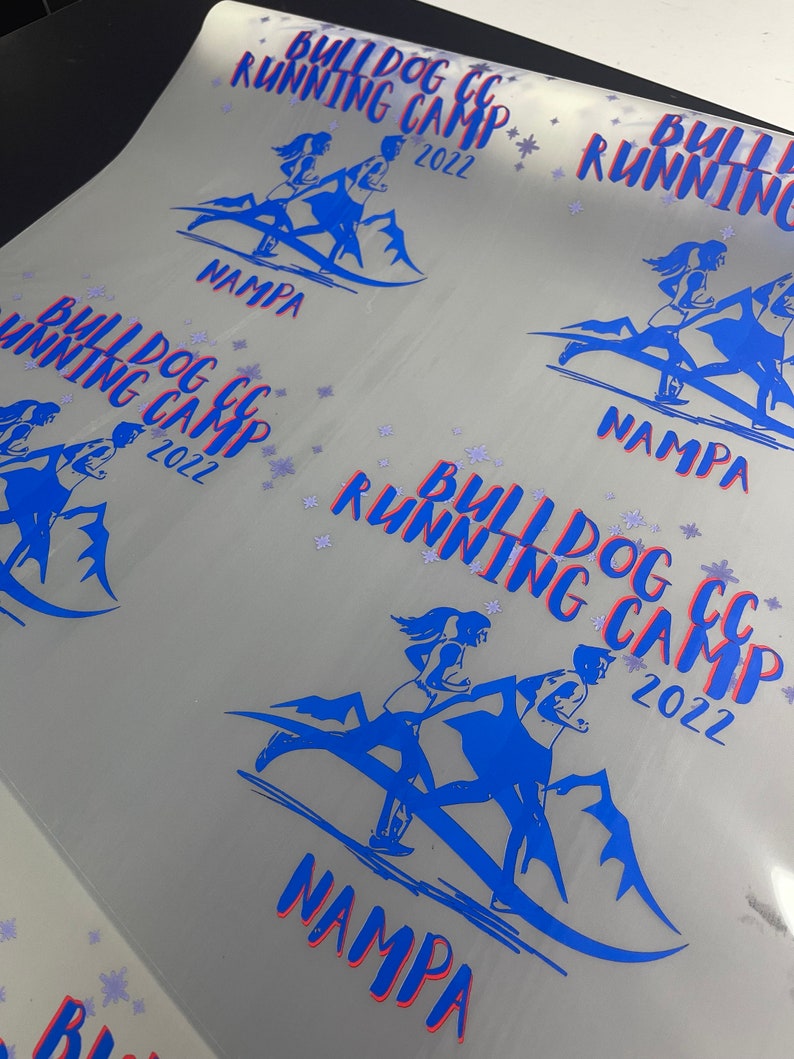 Puede incluir: Una hoja de papel blanca con varios dise&ntilde;os azules y rojos impresos en ella. Los dise&ntilde;os muestran a un grupo de personas corriendo en una monta&ntilde;a con el texto "Bulldog CC Running Camp 2022" y "Nampa" impreso debajo.
