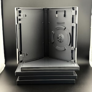 May include: A stack of four black plastic DVD cases, with the top case standing open to reveal an empty interior featuring a central disc hub, side clips for holding paper inserts, and a hinged spine structure for secure storage.