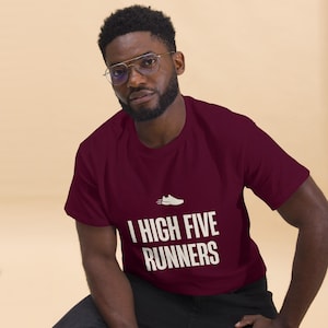 May include: A maroon short-sleeved t-shirt featuring a small white graphic of a running shoe above the text "I HIGH FIVE RUNNERS" printed in white capital letters across the center of the chest area of the garment.