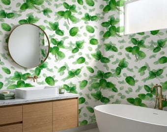 May include: Wallpaper featuring a repeating pattern of green watercolor-style leaves on a white background. The design covers the walls of a bathroom containing a white freestanding bathtub, a wooden vanity, and a round mirror.