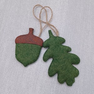 May include: A felt acorn and oak leaf ornament set with a brown felt acorn and a green felt oak leaf. The ornaments are attached to a twine string.