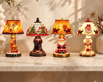 Puede incluir: Cuatro lámparas de mesa decorativas con temas festivos. La primera tiene una base y pantalla de reno. La segunda es una lámpara estilo vitral con árboles. La tercera presenta una base de Santa Claus y una pantalla con patrón de regalos.