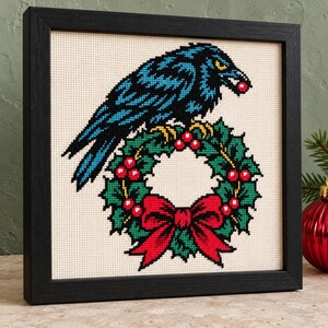 Raven wreath cross stitch in a black frame on a shelf