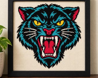 May include: A framed cross-stitch embroidery featuring the head of a snarling panther. The design uses black, teal, and red thread on a cream-colored fabric background. The panther has bright yellow eyes, white fangs, and a red mouth.