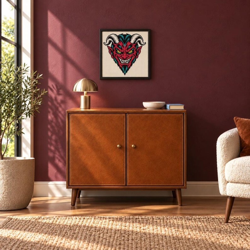 May include: A rectangular brown leather cabinet with two doors, each featuring a small round knob. Above the cabinet hangs a square framed print displaying a graphic illustration of a red-faced devil with horns, yellow eyes, and sharp teeth.