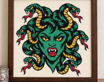 Puede incluir: Un bordado en punto de cruz enmarcado que muestra una figura de piel verde con ojos amarillos y colmillos, rodeada de varias serpientes verdes y amarillas con lenguas rojas sobre un fondo de tela color crema.