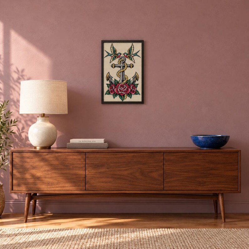 May include: A framed wall art print featuring a central gray anchor wrapped in a yellow rope, flanked by two colorful swallows at the top and three red roses with green leaves at the base, all set against a cream-colored background.