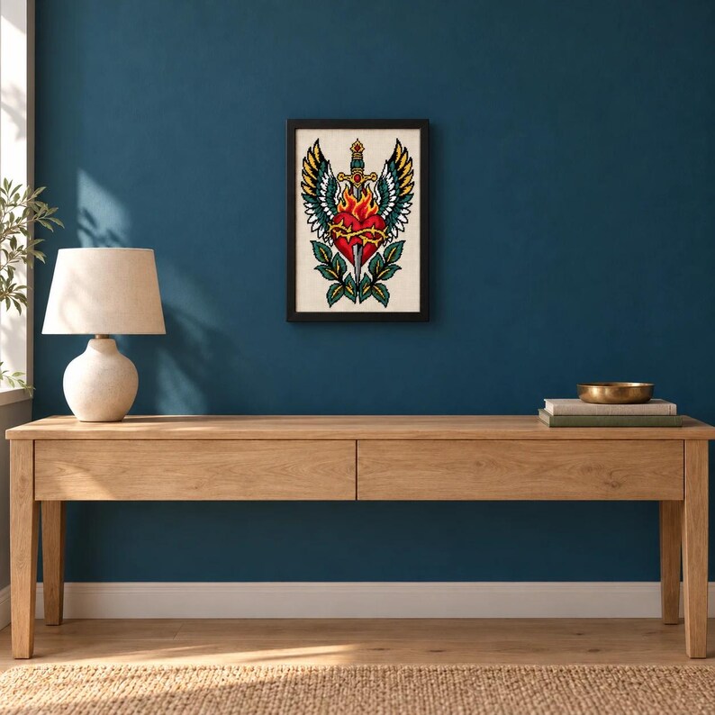 Framed winged sacred heart with dagger cross stitch on a wall