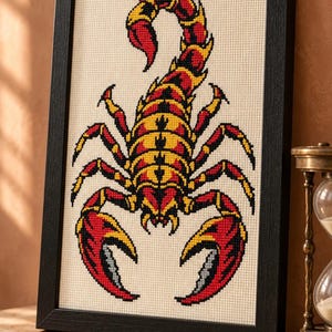 Scorpion cross stitch in a tall black frame on a shelf