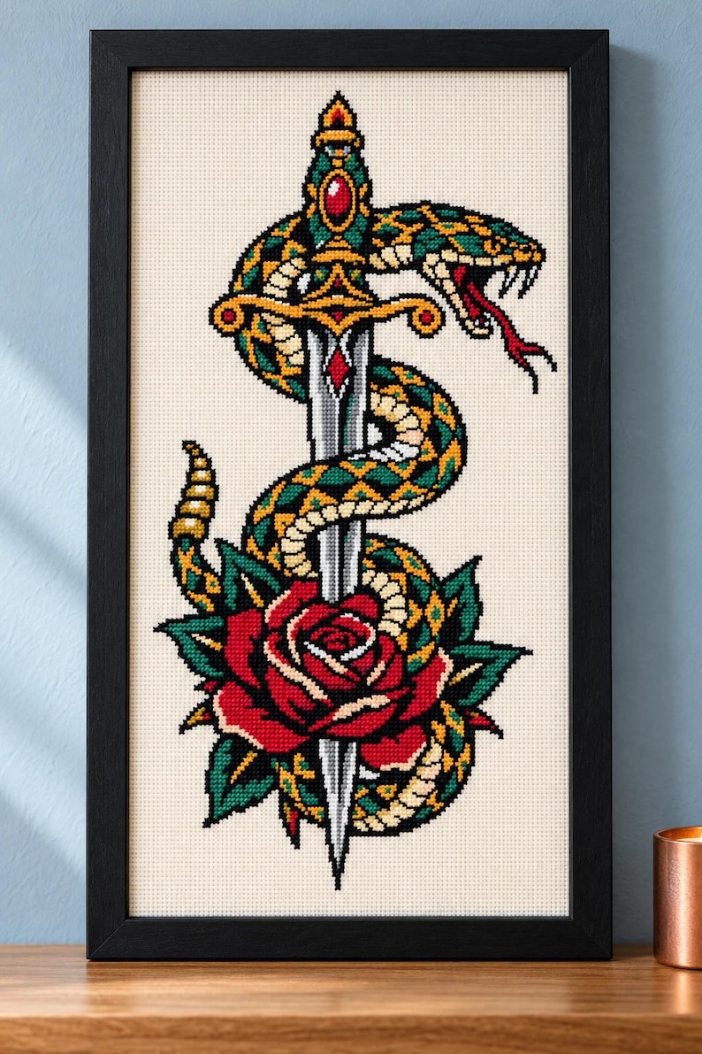 Straight-on view of the finished Snake and Dagger Cross Stitch in a black frame on a wooden shelf