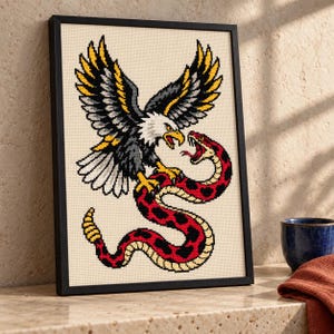 Eagle and snake cross stitch in a tall black frame on a shelf