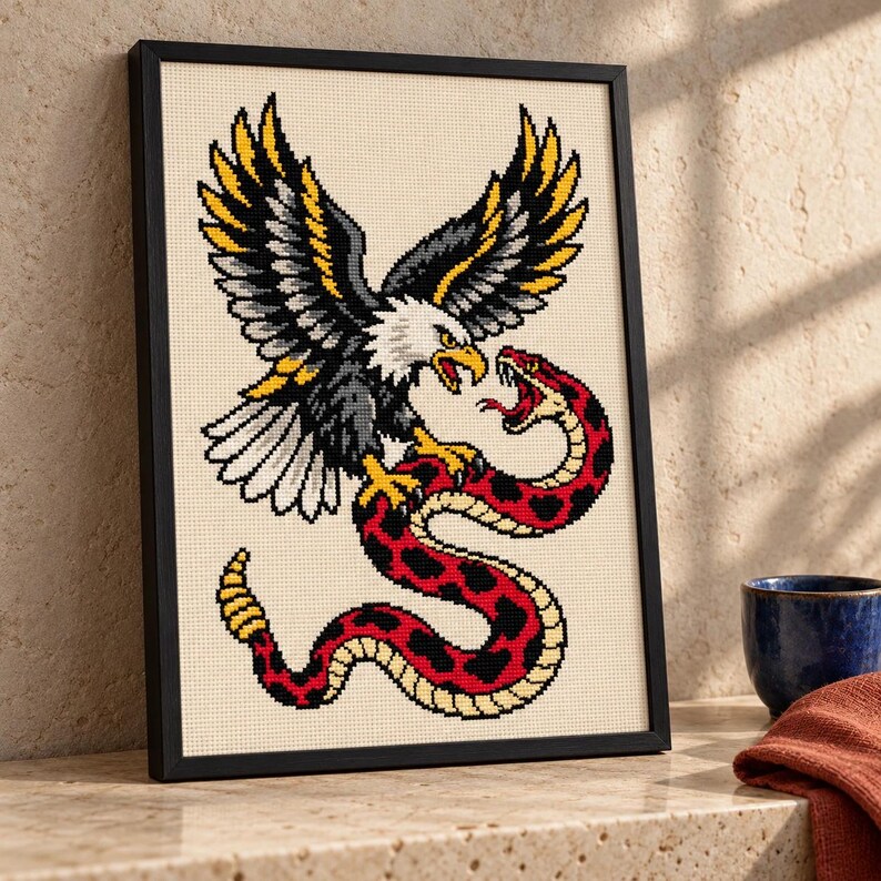Eagle and snake cross stitch in a tall black frame on a shelf