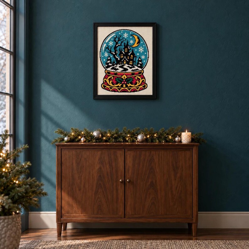 Framed haunted house snow globe cross stitch on a wall