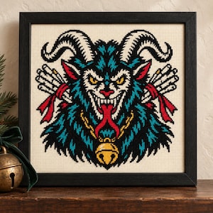 Straight-on view of the finished Krampus Cross Stitch in a black frame on a wooden shelf