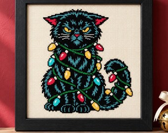 May include: A framed cross-stitch embroidery featuring a black cat with yellow eyes and pink inner ears, wrapped in a string of colorful red, yellow, and blue Christmas lights. The cat has a grumpy expression and is set against a cream fabric background.