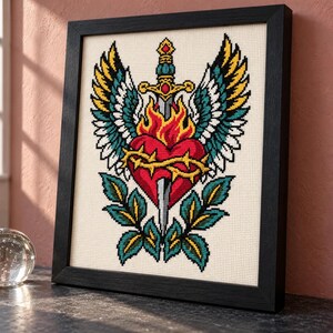Sacred heart cross stitch in a tall black frame on a shelf