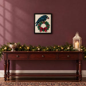 Framed raven on a holly wreath cross stitch on a wall