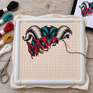 Devil head cross stitch in progress on a scroll frame with floss and scissors