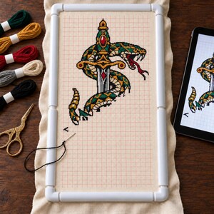 Snake and dagger cross stitch in progress with floss and scissors